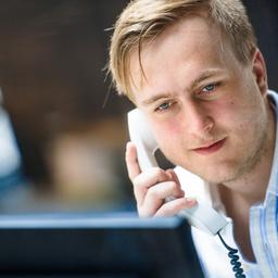 Berufseinsteiger: Junger Mann mit Telefonhörer vor Bildschirm
