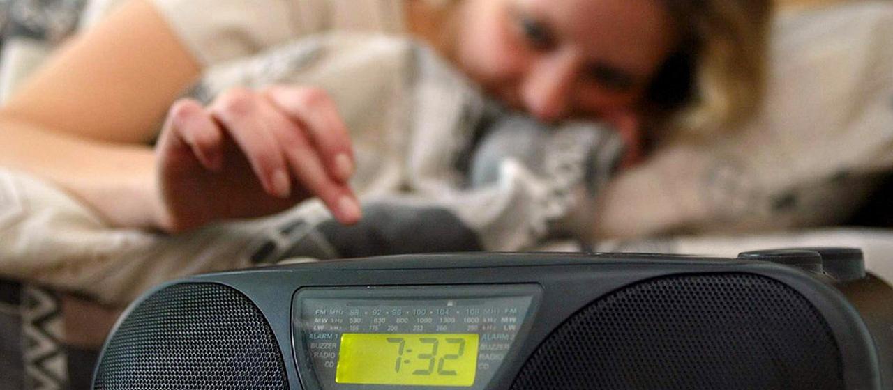 Frau schaltet Radiogerät am Bett ein